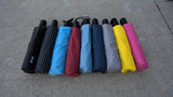 A photo of a lineup of many different colored umbrellas lying on a sidewalk. 