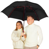 A photo of a smiling couple in matching white sweaters under a large black umbrella with red spokes. 