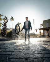 An artistic photo of a man facing the camera with the sun behind him holding an umbrella in a plaza. 