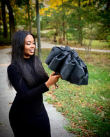 A photo of a woman outside looking like she's about to open her black umbrella.