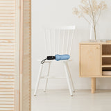 A photo of the interior of a neutral colored room in a home with a closed, light blue travel umbrella resting on a char. 