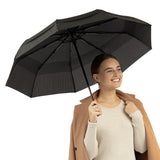 A woman holding the windproof travel compact umbrella by Repel Umbrella in pin stripe