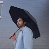 A man in a blue button down, outdoors in front of a tiled building holding his best-selling Repel Wind-proof and durable sturdy compact travel umbrella